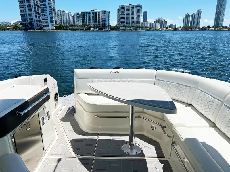 Slide: The Image of 2019 Sea Ray Sundancer 320 Outboard interior with seating, table, and waterfront cityscape. - 14