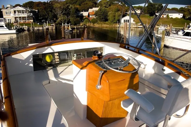 Slide: The Image of 1957 Rybovich Convertible boat helm with wooden steering, docked in a scenic marina. - 3