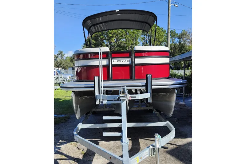 Slide: The Image of 2026 Lowe SS 230 DV pontoon boat on trailer, red and white design, parked outdoors. - 2