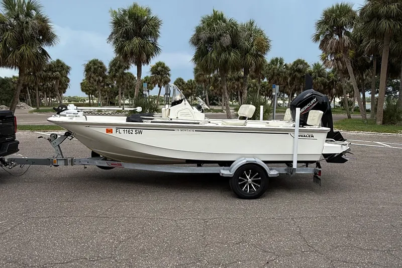 Slide: The Image of 2021 Boston Whaler 170 Montauk boat on trailer, parked near palm trees. - 2