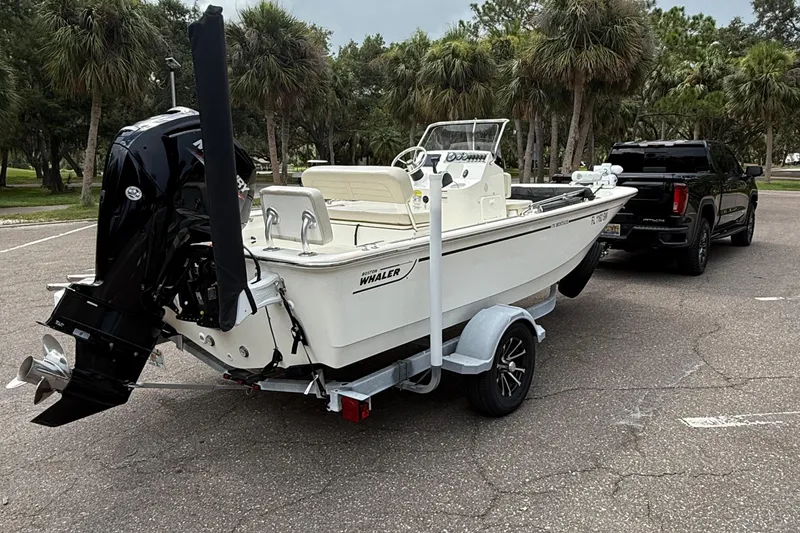 Slide: The Image of 2021 Boston Whaler 170 Montauk boat on trailer, parked near black truck, surrounded by trees. - 5
