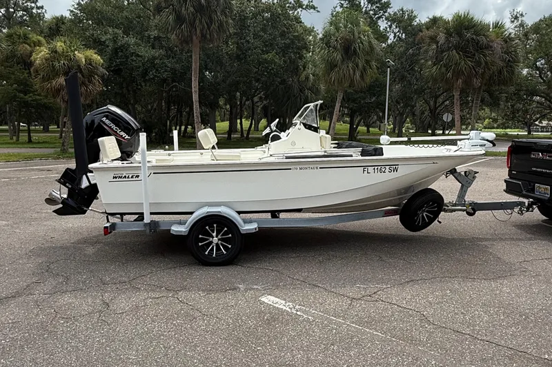 Slide: The Image of 2021 Boston Whaler 170 Montauk boat on trailer, parked outdoors with trees in background. - 6