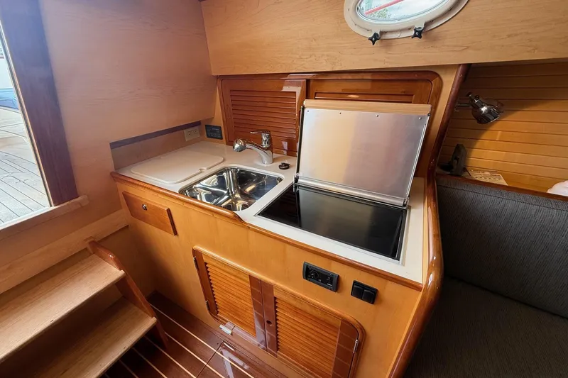 Slide: The Image of Compact galley in 2015 Hinckley DS 42 yacht with sink, stove, and wooden cabinetry. - 63