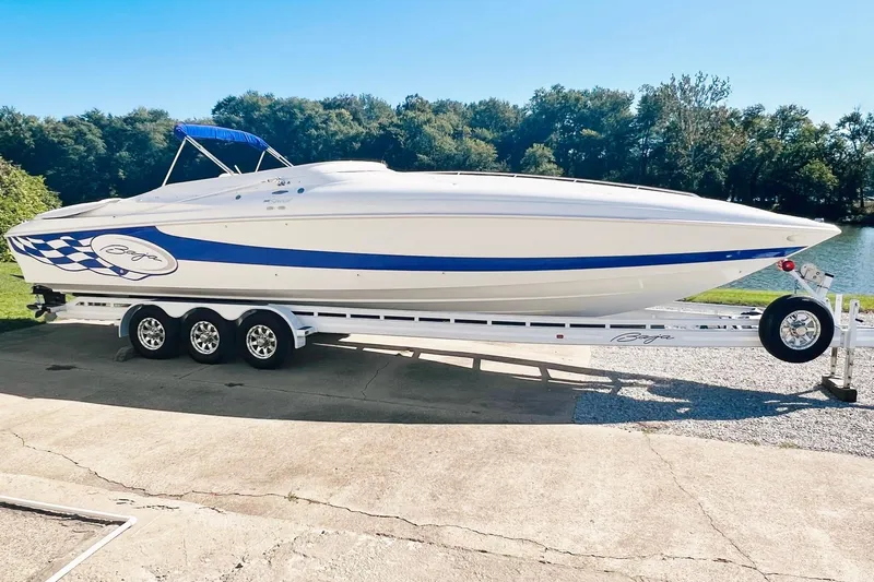 Slide: The Image of 1996 Baja .38 Special boat on trailer, white with blue accents, parked near a lake. - 1