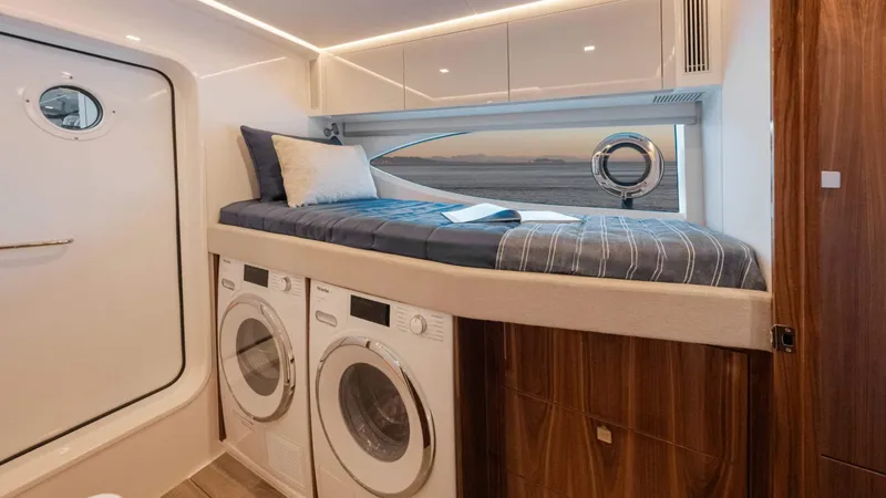 Slide: The Image of 2025 Riviera 6800 Sport Yacht interior with bed, washer, dryer, and porthole window. - 35