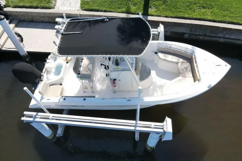 Slide: The Image of 2023 Cobia 217 CC boat with black canopy docked on a lift. - 2