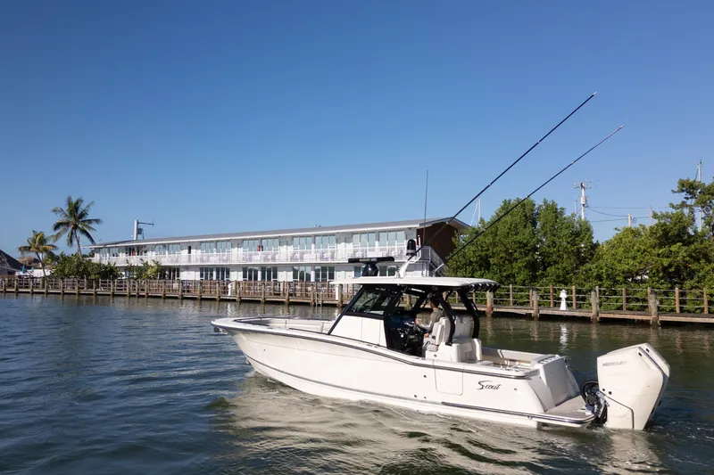 Slide: The Image of 2024 Scout 330 LXF boat cruising near waterfront building under clear blue sky. - 15