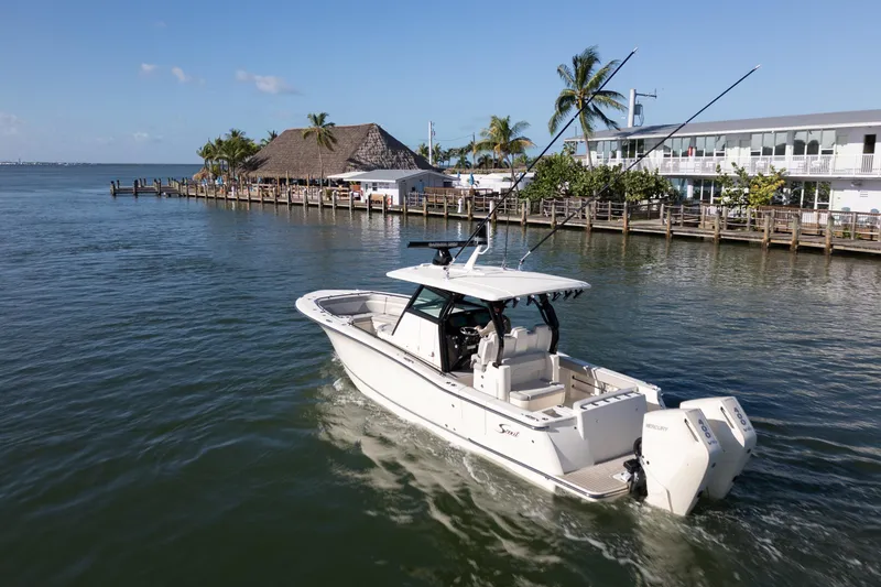 Slide: The Image of 2024 Scout 330 LXF boat cruising near a tropical waterfront with palm trees. - 7