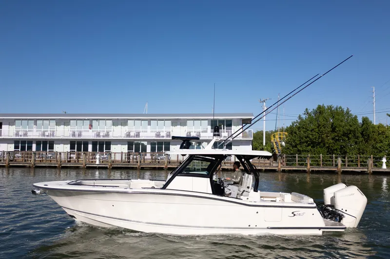 Slide: The Image of 2024 Scout 330 LXF boat cruising on water near a modern waterfront building. - 8