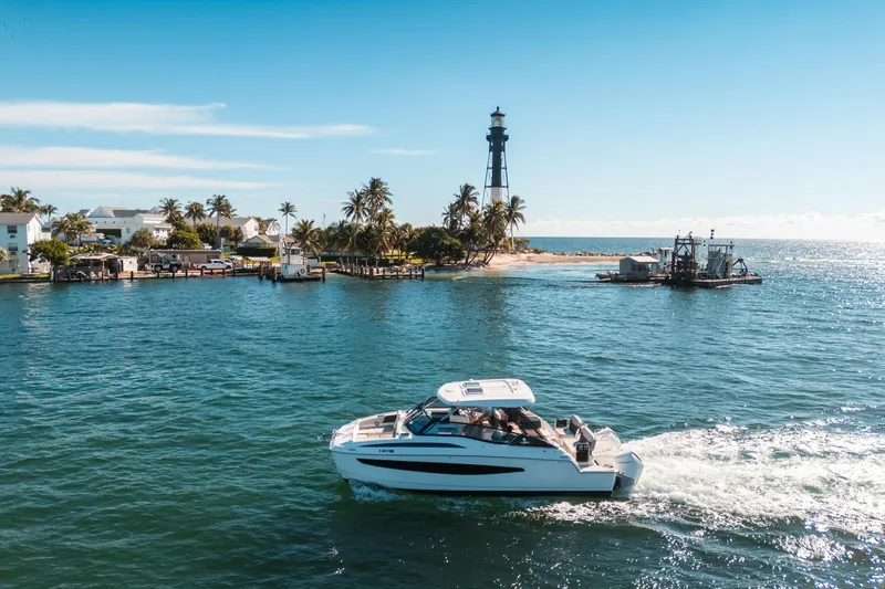 Slide: The Image of Aquila 32 Sport 2022 cruising near a lighthouse and palm-lined shore. - 48