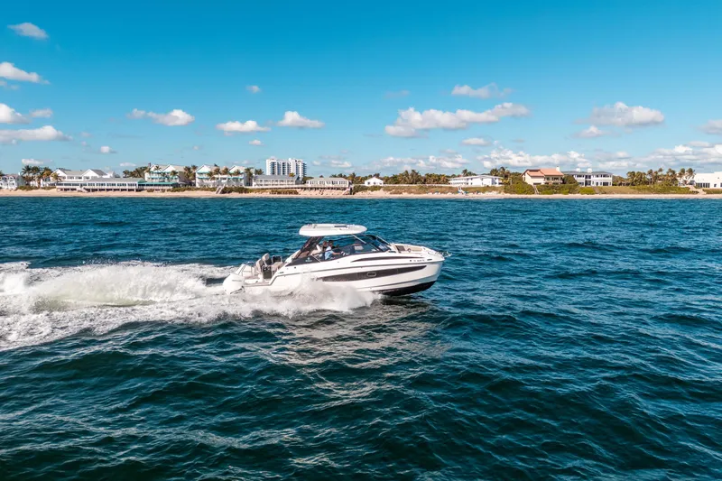 Slide: The Image of Aquila 32 Sport 2022 cruising on ocean near coastal homes under blue sky. - 56