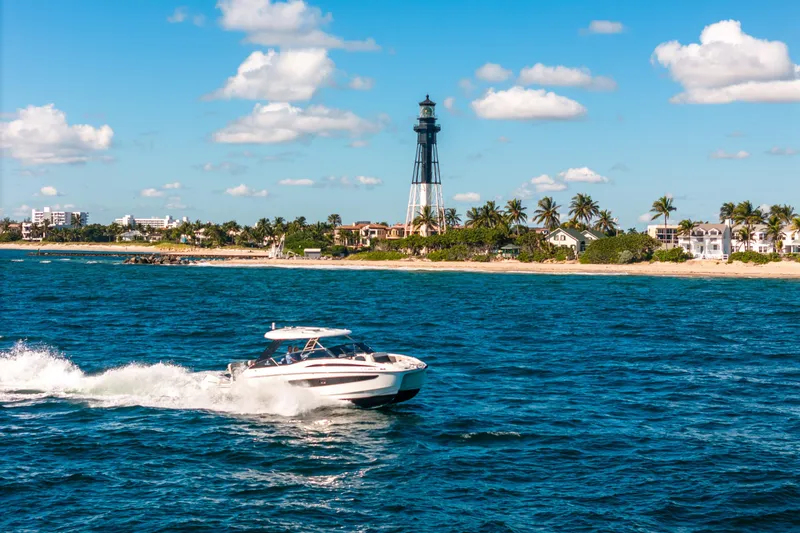 Slide: The Image of Aquila 32 Sport 2022 cruising near a coastal lighthouse under a clear blue sky. - 61