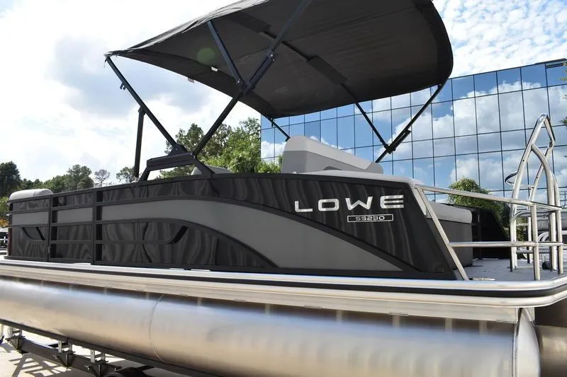 Slide: The Image of 2023 Lowe SS 230 DV pontoon boat with canopy, parked near reflective building. - 6