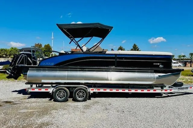 The Image of 2025 Harris Cruiser 250 pontoon boat on a trailer under a clear blue sky. - 0