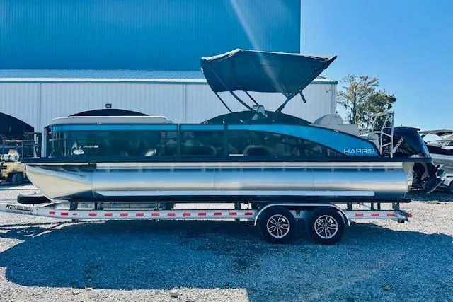 Slide: The Image of 2025 Harris Cruiser 250 pontoon boat on trailer, parked outdoors under blue sky. - 4