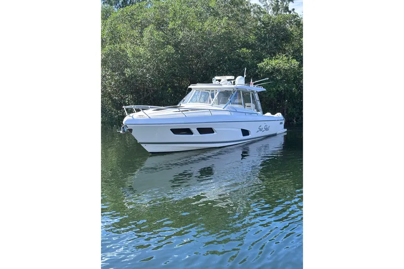 Slide: The Image of 2020 Intrepid 409 Valor boat on calm water, surrounded by lush greenery. - 10