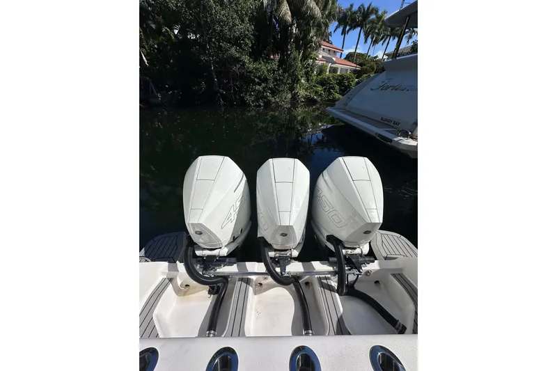 Slide: The Image of Triple outboard engines on a 2020 Intrepid 409 Valor boat, docked near lush greenery. - 30