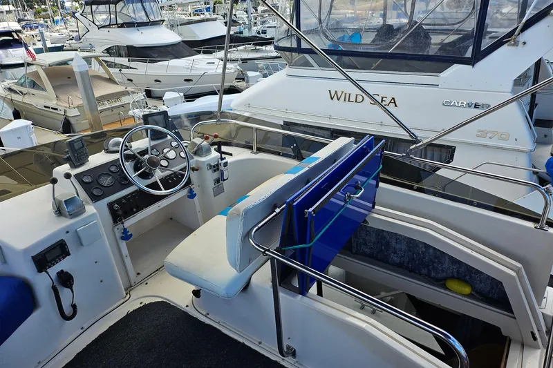 Slide: The Image of 1988 Silverton 37 Motor Yacht helm with marina view, featuring steering wheel and control panel. - 10