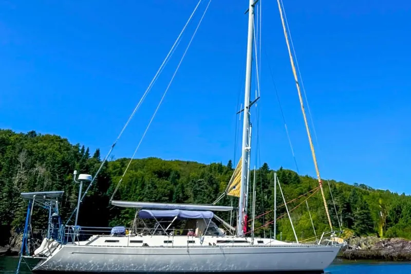 The Image of Sailboat Oyster LW48, 1991 model, anchored near lush green forest under clear blue sky. - 0