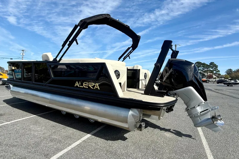 Slide: The Image of 2026 Alera M23 pontoon boat with Mercury outboard motor, parked on asphalt under blue sky. - 6