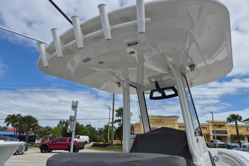Slide: The Image of 2026 Regulator 23 boat with T-top and rod holders, parked near shops under a cloudy sky. - 14