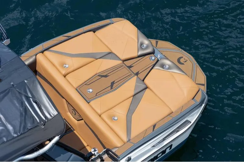 Slide: The Image of 2025 Centurion Nv233 boat with tan and gray cushioned deck on water. - 21