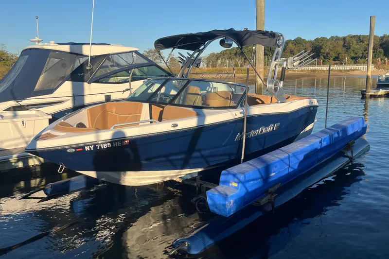 Slide: The Image of 2021 MasterCraft XT21 boat docked on water with blue hull and tan interior. - 2