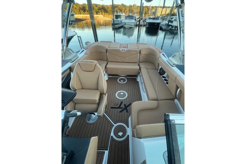 Slide: The Image of 2021 MasterCraft XT21 boat interior with tan seating and wood-style flooring at a marina. - 21