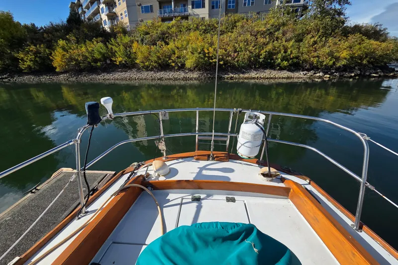Slide: The Image of 1982 Cape Dory 33 sailboat deck with railing, docked near lush greenery and buildings. - 6