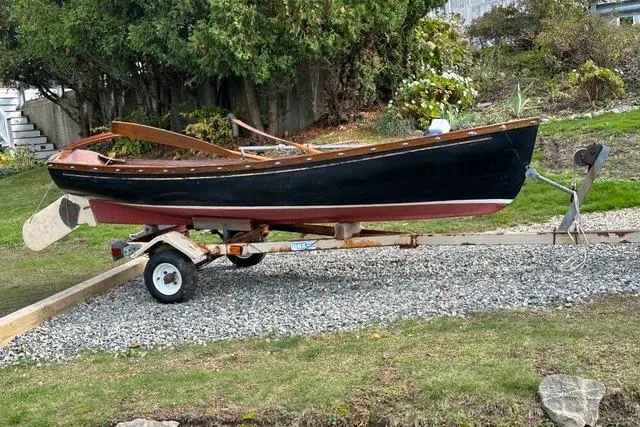 Slide: The Image of 1974 Jarvis Newman rowing/sailing dinghy on trailer, displayed outdoors on gravel path. - 0