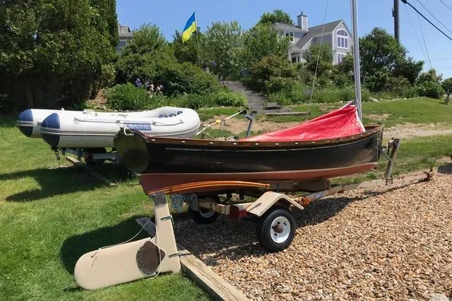 Slide: The Image of 1974 Jarvis Newman Dinghy on trailer, with red cover, near a house and greenery. - 1