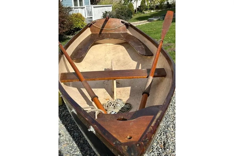Slide: The Image of 1974 Jarvis Newman rowing/sailing dinghy with wooden oars, displayed outdoors on gravel. - 2