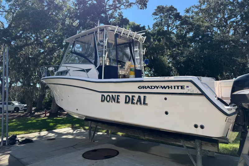 The Image of 1998 Grady-White Marlin 300 boat on a lift, named "Done Deal," surrounded by trees. - 0