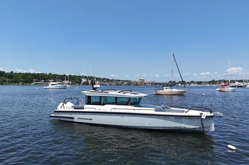 Slide: The Image of 2026 Axopar 37 XC Cross Cabin boat on a serene lake with sailboats. - 8