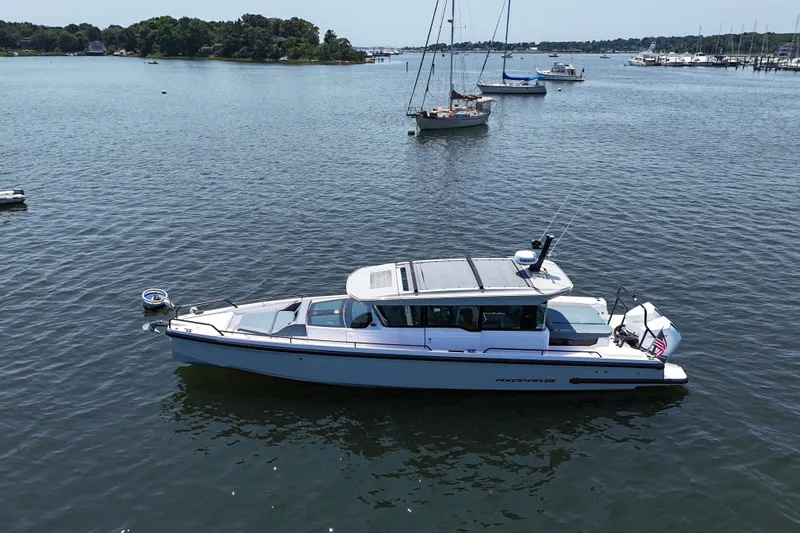 Slide: The Image of 2026 Axopar 37 XC Cross Cabin boat on calm water with sailboats in the background. - 9