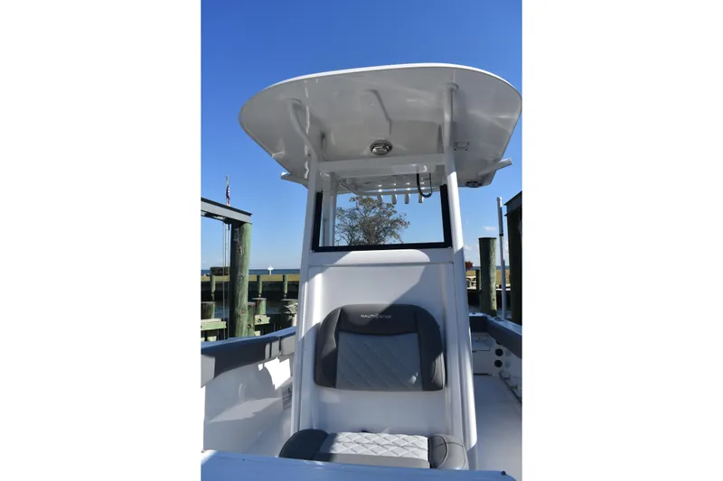 Slide: The Image of 2025 NauticStar 242L Offshore boat interior with seating and T-top under clear blue sky. - 48