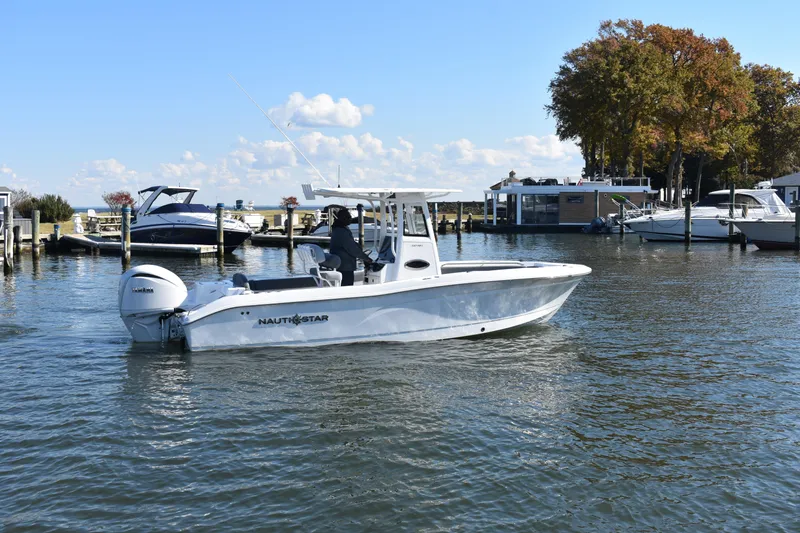 Slide: The Image of 2025 NauticStar 242L Offshore boat cruising in a scenic marina setting. - 57