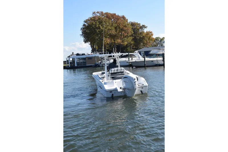 Slide: The Image of 2025 NauticStar 242L Offshore boat cruising on a calm lake near a marina. - 62