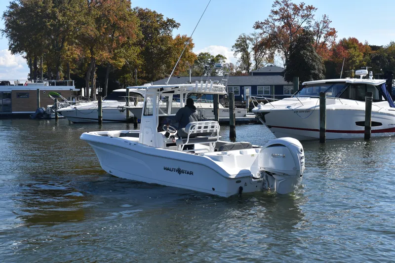 Slide: The Image of 2025 NauticStar 242L Offshore boat cruising in a marina with surrounding yachts. - 64