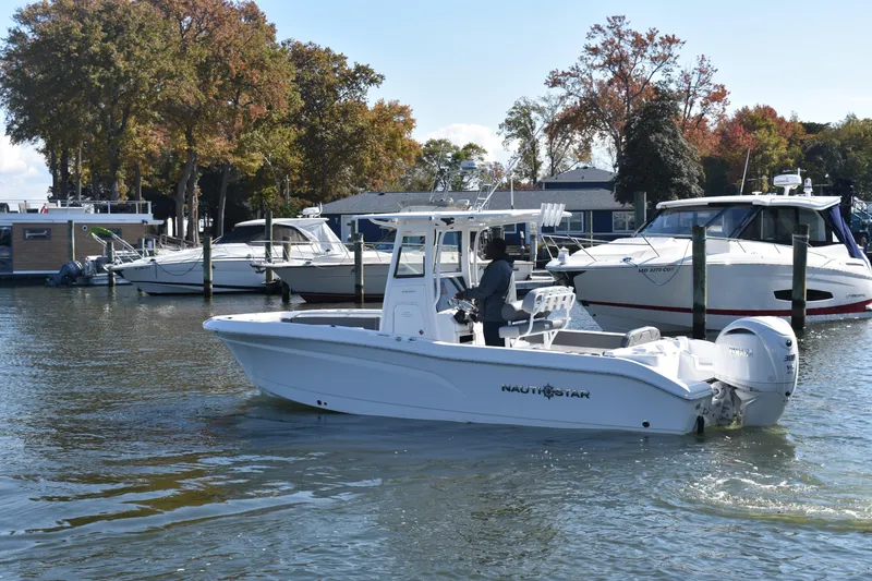 Slide: The Image of 2025 NauticStar 242L Offshore boat cruising in a marina with autumn trees. - 65