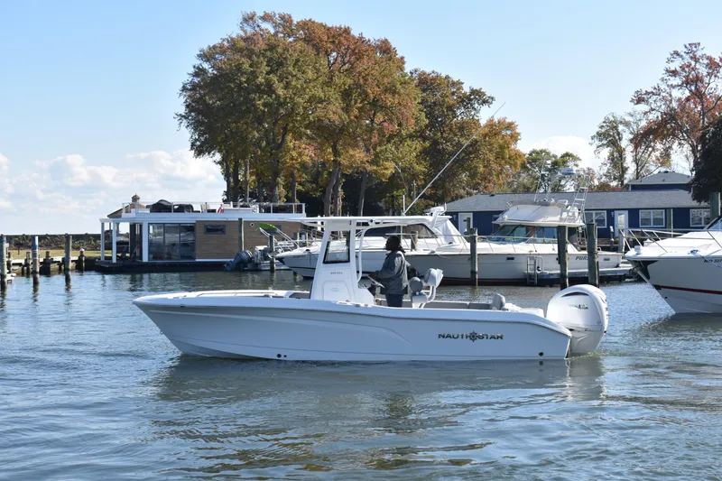 Slide: The Image of 2025 NauticStar 242L Offshore boat cruising near docks with autumn trees in the background. - 66