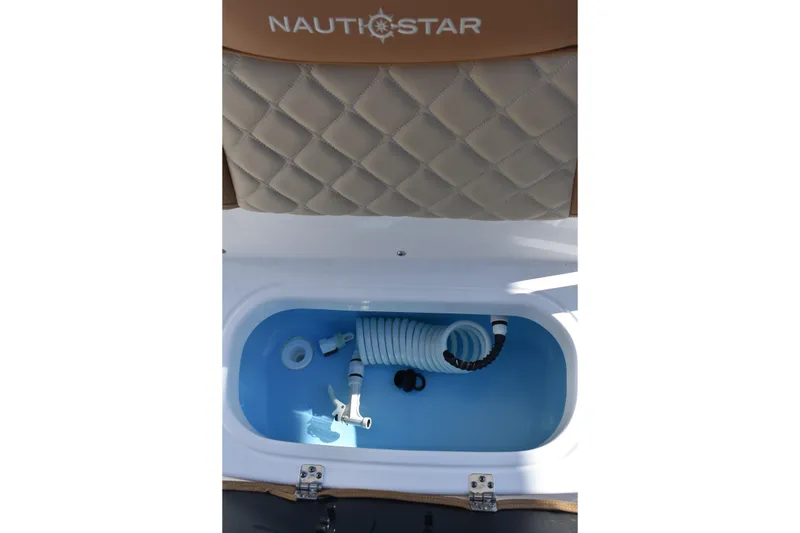 Slide: The Image of 2025 NauticStar 231 Hybrid boat storage compartment with coiled hose and beige cushioned seat. - 32