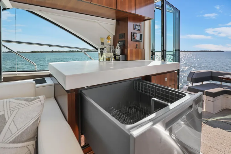 Slide: The Image of Luxurious 2022 Cruisers Yachts 54 Cantius interior with bar and dishwasher, overlooking serene waters. - 42