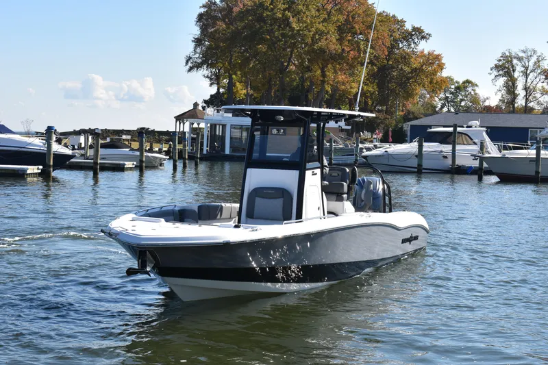 Slide: The Image of 2025 NauticStar 251 Hybrid boat cruising in a marina with surrounding docks and trees. - 64