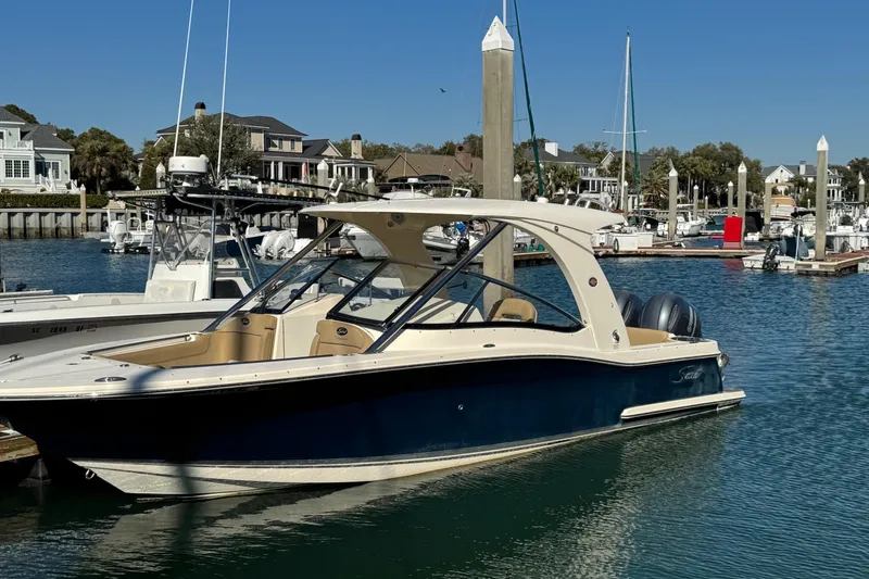 Slide: The Image of 2015 Scout 275 Dorado boat cruising on a sunny waterfront with docks and houses. - 0