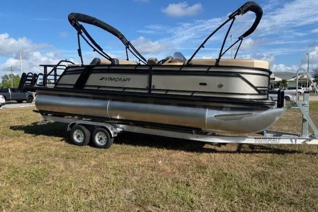 The Image of 2026 Starcraft EXS 3 DL pontoon boat on trailer, parked on grass under blue sky. - 0