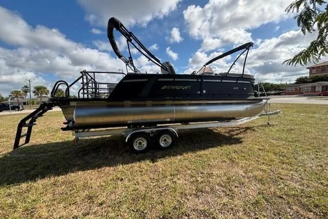 Slide: The Image of 2026 Starcraft EXS 3 Q DH pontoon boat on trailer, parked on grass under cloudy sky. - 4