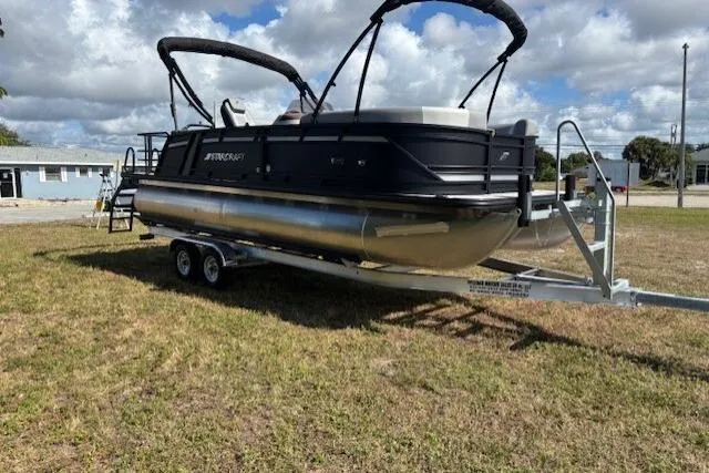 Slide: The Image of 2026 Starcraft EXS 3 Q DH pontoon boat on trailer, parked on grass under cloudy sky. - 5
