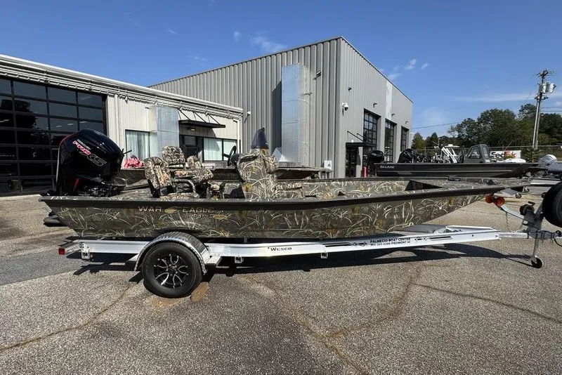 Slide: The Image of 2026 War Eagle 961 Blackhawk boat on trailer, camo design, parked outside dealership. - 3