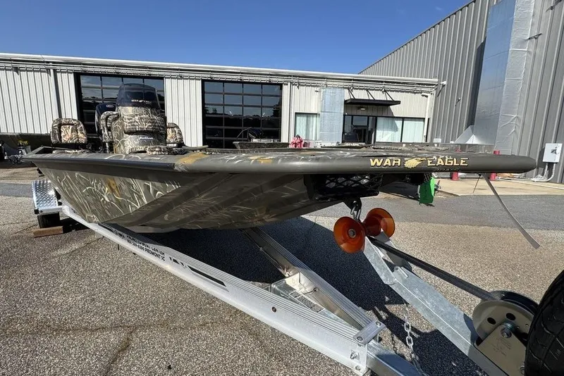 Slide: The Image of 2026 War Eagle 961 Blackhawk boat on trailer, camo design, parked outside industrial building. - 7